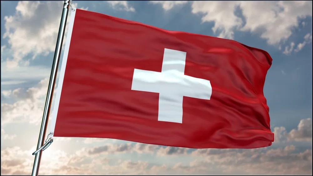 La bandera suiza ondeando al viento con los Alpes suizos al fondo, simbolizando la excelencia de la educación gastronómica en Suiza.