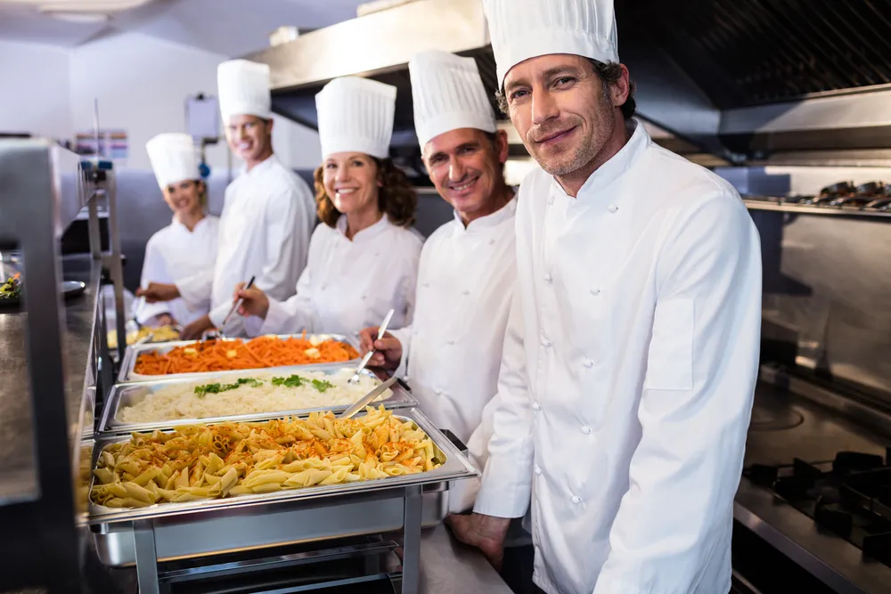 Chefs preparing food in a catering kitchen with stainless steel countertops and commercial kitchen equipment. The team is led by a Cordon Bleu trained chef.