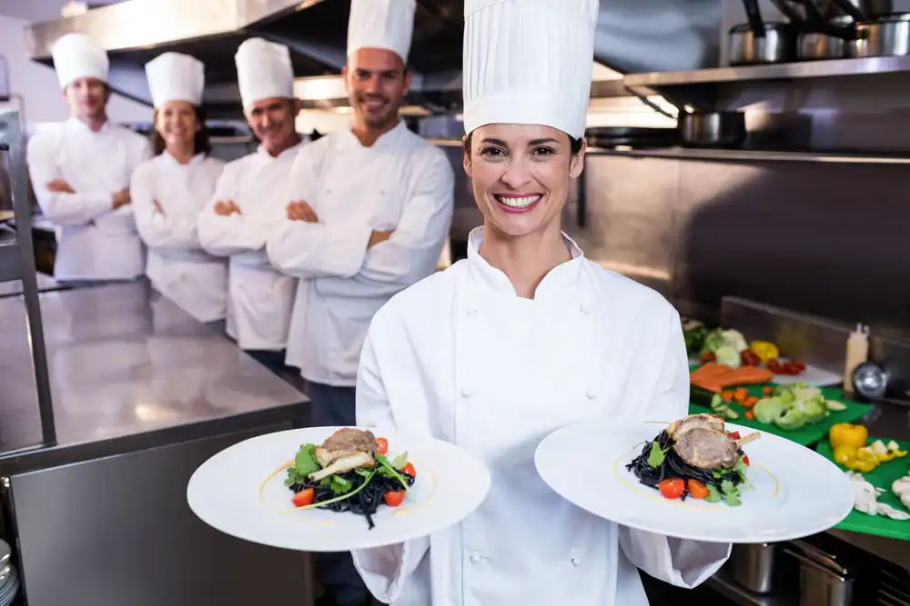 A group of culinary students in a professional kitchen show off two dishes they prepared. The best culinary schools in France teach you the skills you need to succeed in the culinary world.