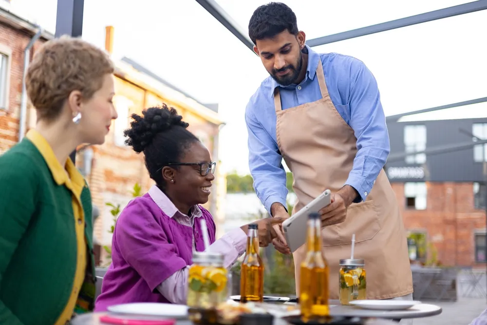 A waiter in a restaurant explaining how to leave a review on Google Reviews or Yelp.