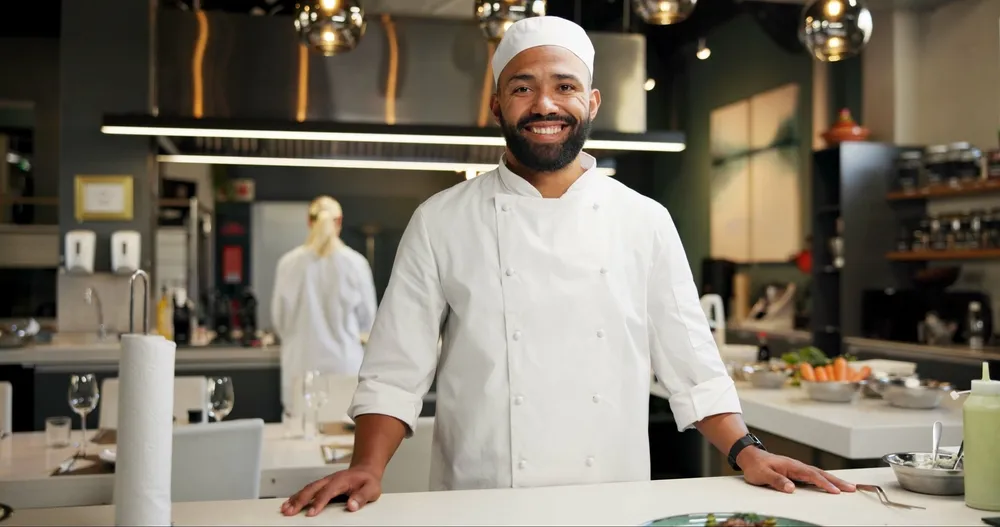 A smiling chef poses for a photo in a restaurant kitchen. Digital marketing on TikTok for restaurants can include highlighting the team behind the counter.