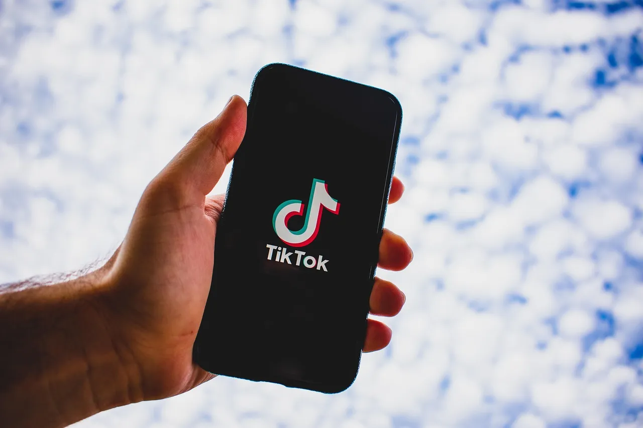 A hand holds up a mobile phone with a TikTok video of his restaurant about to play. Digital marketing on TikTok for restaurants can include behind-the-scenes videos.