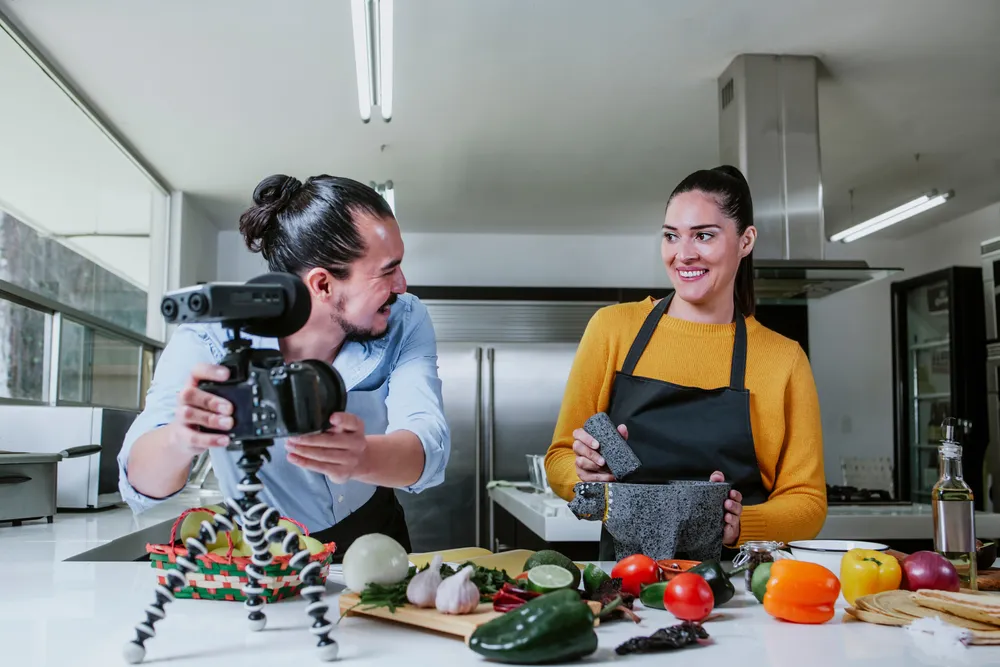 Two YouTube content creators filming a cooking video in a restaurant kitchen. With a basic camera and tripod, you can go a long way in creating engaging video content for your restaurant's YouTube channel.