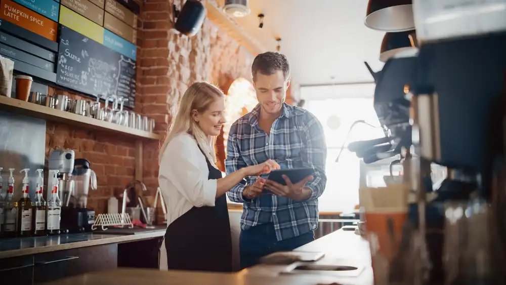 A restaurant owner and her general manager looking at a tablet computer with a Google Ads dashboard on the screen showing increased sales and revenue at their restaurant.
