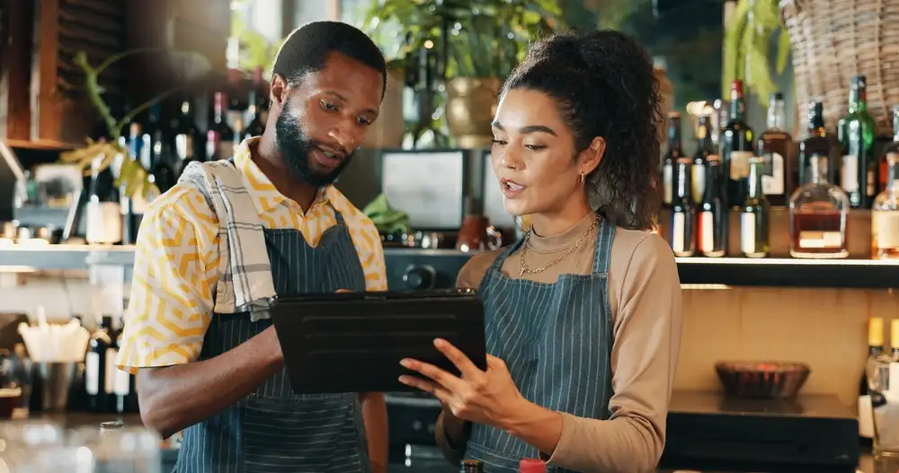 Un gerente de restaurante necesita saber cómo calcular el costo de la comida del restaurante para determinar los mejores precios para los artículos de su menú, como se muestra en esta imagen de dos gerentes de restaurante calculando los costos de la comida en una tableta.