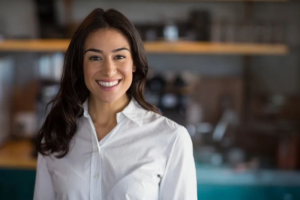 The owner of a cafe business poses confidently in front of her cafe, ready to welcome customers. Follow our practical tips to start your own cafe business successfully.