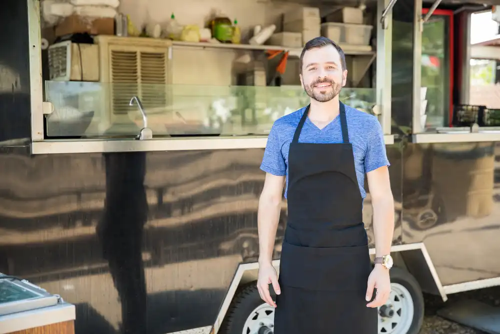 A new food truck owner stands in front of his food truck, ready to serve customers.
