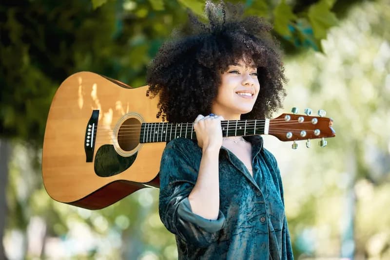 A female musician with her guitar slung over shoulder enjoying the outdoor scenery in Nashville, Tennessee. She is on the lookout for a food truck to grab a bite to eat.