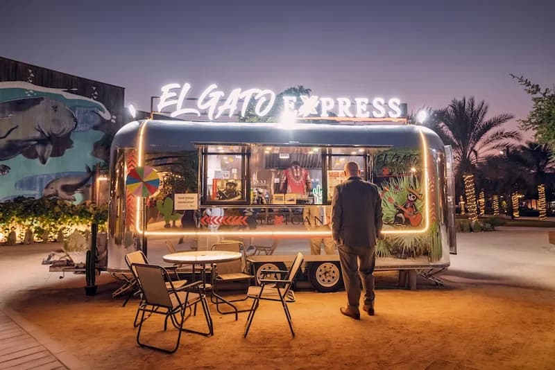 A customer stands outside a food truck with folding tables and chairs set up nearby. Adding seating can enhance customer comfort when running a food truck business in Nashville, Tennessee.