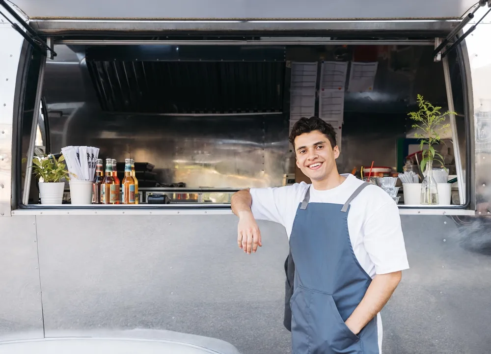 A food truck owner in Orlando, FL, is preparing to start his leaning against his food truck on a quick break. Starting a food truck business in Orlando, FL, requires several steps, including obtaining the necessary permits and licenses.