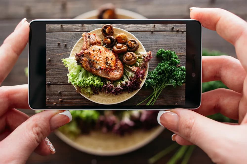 La dueña de un restaurante usa su smartphone para tomar una foto del menú de un delicioso plato. Fotos de calidad para el menú del restaurante pueden aumentar las ventas en línea en un 35 %.