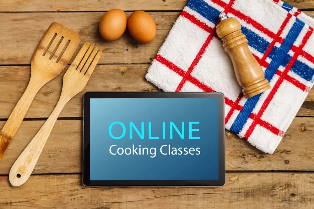 A table that says Online Cooking Classes with wooden spoons an forks, eggs, and a kitchen towel with black pepper grinder. Online cooking classes can help you become a better cook.
