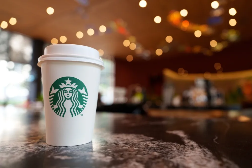 The Starbucks coffee cup with the iconic green siren logo on it. Starbucks is a global coffeehouse chain known for its specialty coffee drinks, cozy ambiance, and commitment to sustainability.