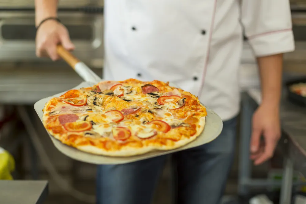 A culinary instructor preparing pizza in a traditional Italian kitchen at the Italian Culinary Institute for Foreigners.