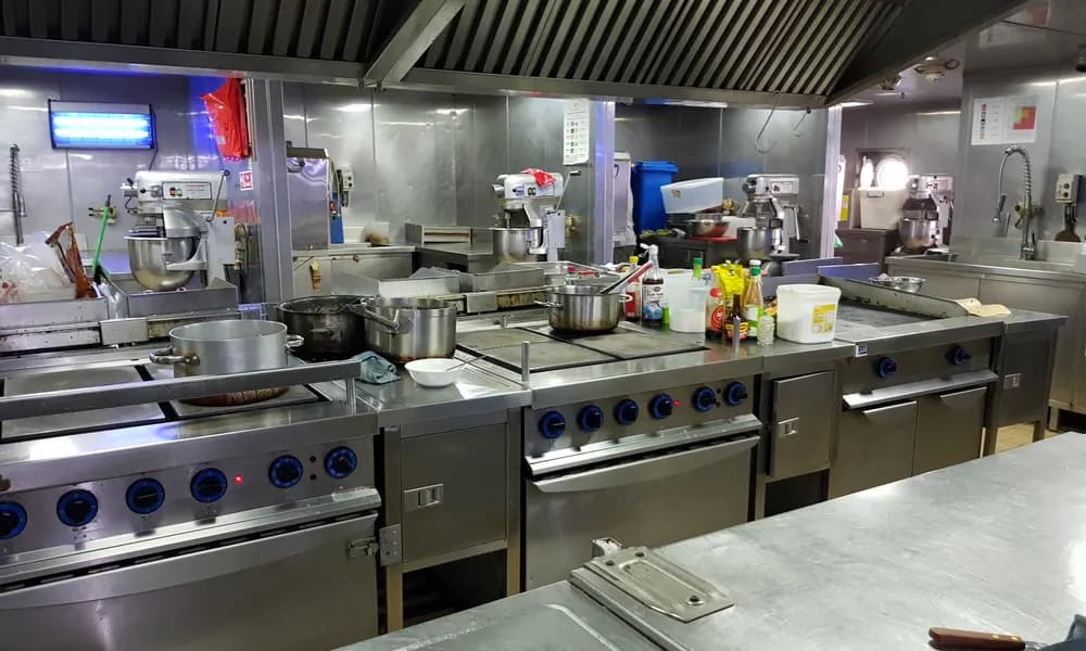 A commercial kitchen full of various equipment, including ovens, refrigerators, and prep tables. Buying used commercial kitchen equipment can be a smart investment with proper maintenance.