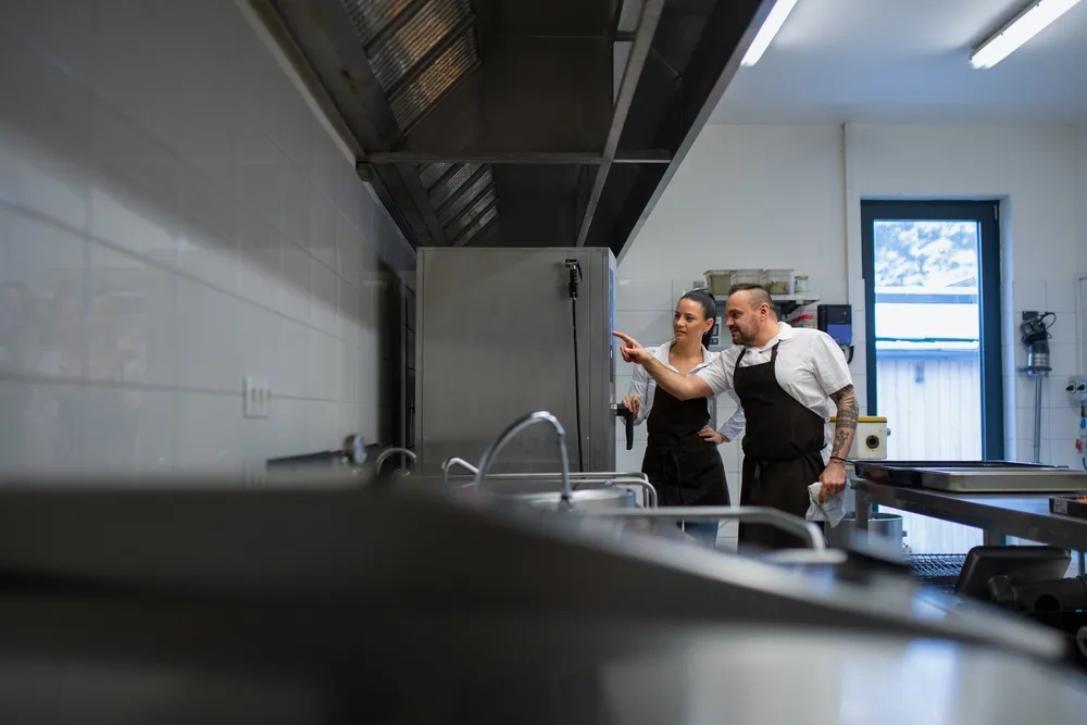 Two chefs inspect kitchen equipment in their restaurant kitchen. Buying used commercial kitchen equipment can save restaurant owners thousands of dollars when opening a new restaurant.