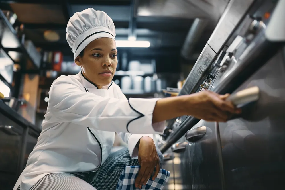 A chef inspects the handles on a piece of used commercial kitchen equipment before purchasing it. Buying used commercial kitchen equipment can save restaurant owners thousands of dollars when opening a new restaurant.
