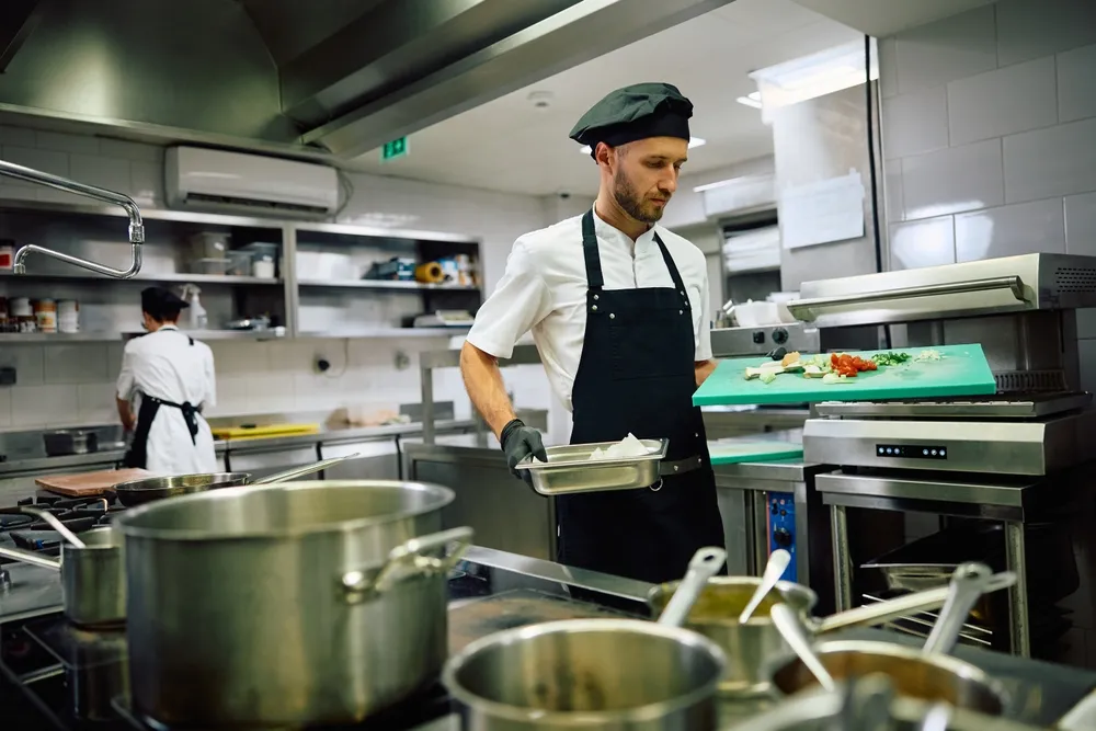 Cooks in a commercial kitchen clean and organize. The kitchen contains both new and used commercial kitchen equipment. Buying used commercial kitchen equipment can save restaurant owners thousands of dollars when opening a new restaurant.