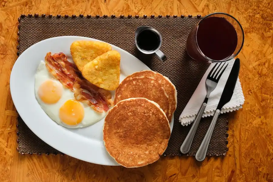 Otra foto de un plato de desayuno con huevos, panqueques y salchichas. Esta imagen del menú tiene un estilo de iluminación y composición diferente en comparación con las dos primeras fotos, creando un estado de ánimo diferente y rompiendo la consistencia visual del menú del restaurante.