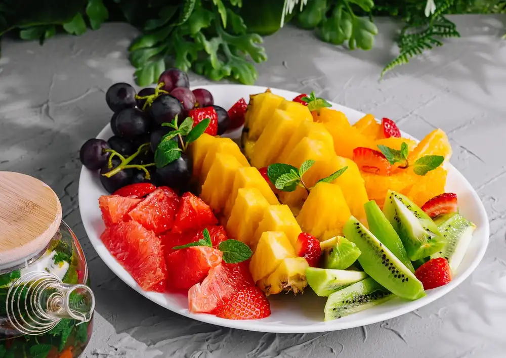 Una bandeja de frutas frescas y variadas está bellamente dispuesta, mostrando una variedad de colores y texturas que la hacen visualmente atractiva. Se debe pensar en una imagen de menú, pero no debe ser excesiva en su estilización.