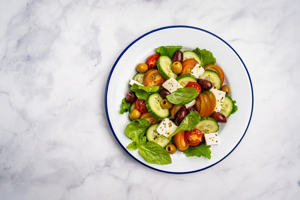 Una fotografía cenital de una ensalada griega. El fondo es limpio y sencillo, lo que convierte al plato en el protagonista de la imagen del menú.