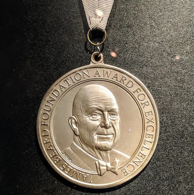 The James Beard Foundation Award for Excellence medallion, symbolizing the prestigious recognition given to outstanding chefs, restaurants, and food professionals in the culinary industry.