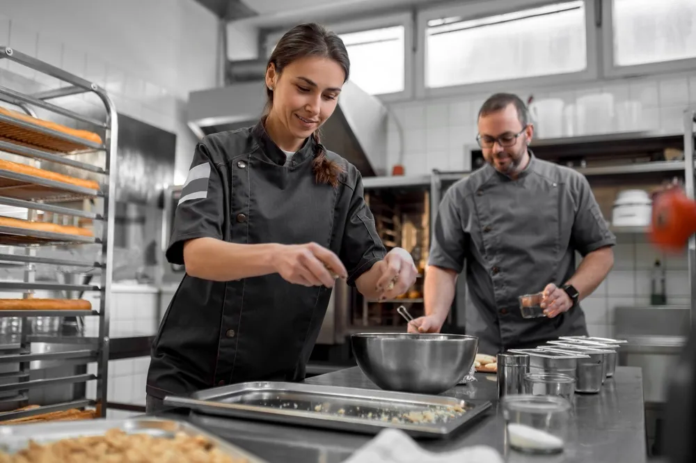 Two chefs are in a professional kitchen preparing gourmet dishes. One chef is plating a dish while the other is adding final touches. The James Beard Awards recognize culinary excellence in the USA.