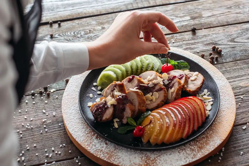 Trabajar como estilista de alimentos es una gran carrera si te encanta el trabajo basado en proyectos que sea emocionante y esté en constante cambio, como se muestra en esta foto de un estilista de alimentos colocando una cereza en un plato de comida para darle el toque final.