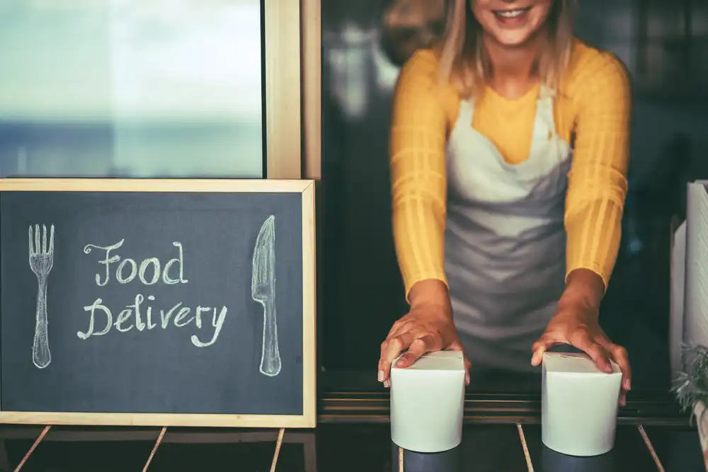 Knowing how to open a ghost kitchen involves understanding what food to serve. As shown in this image of a chef in her ghost kitchen serving prepared food.
