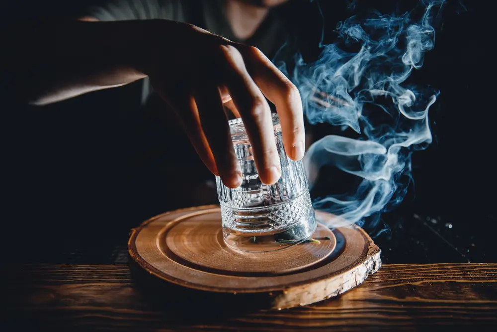 Understanding what is a mixologist is important for restaurants looking to add mixology to their menu. A mixologist is a bartender who specializes in creating unique cocktails and drinks, as shown in this image of a mixologist preparing a cocktail with smoke flavor.