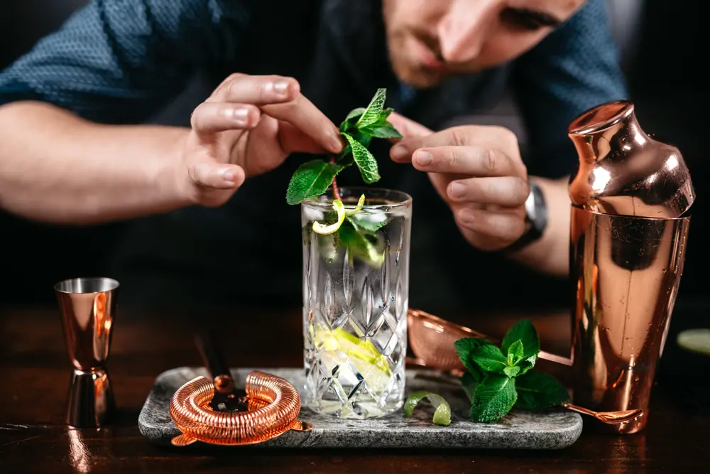 An ultimate mixologist adds a spring of fresh mint to a cocktail, showcasing the importance of training and expertise in mixology. Mixologists often expect higher pay, so budget accordingly.