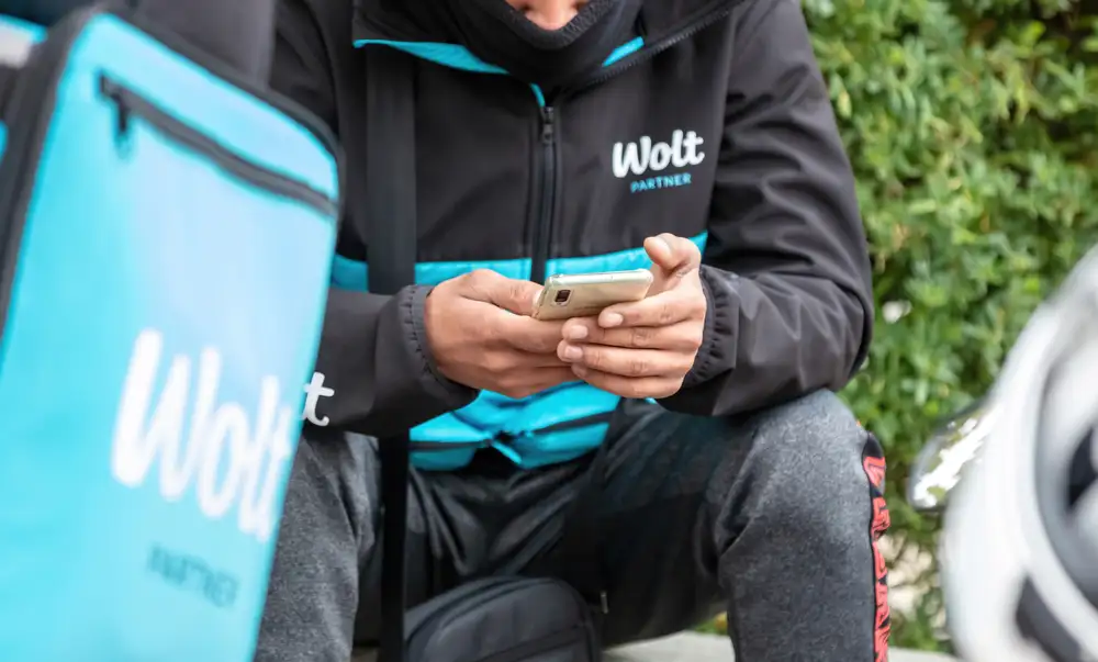Wondering how much are commission fees for Wolt? In the 15% to 30% range, Wolt is one of the best food delivery apps for a restaurant in Europe. As shown in this image of a Wolt delivery bag resting beside its rider in Barcelona, Spain.