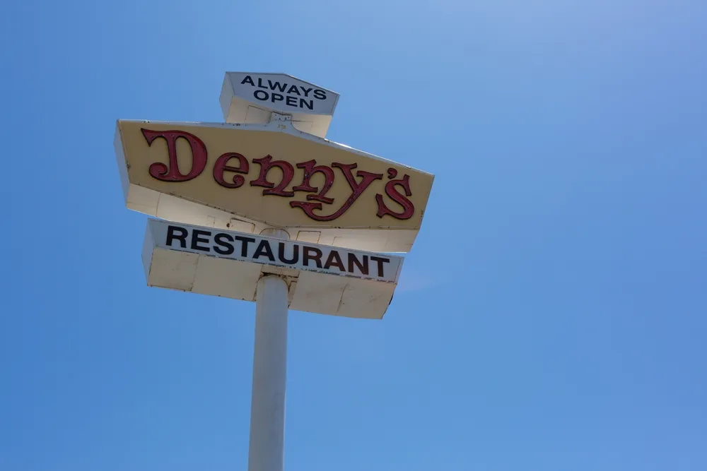 A tall sign for Denny's. Denny's restaurants are strategically located near highways and airports, attracting travelers seeking affordable and reliable dining options.