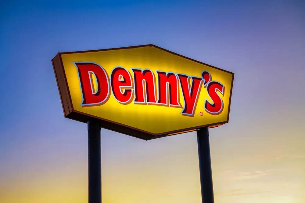 The Denny's sign is illuminated as dusk falls. Denny's commitment to being open 24/7 provides a sense of security and comfort to customers, making it a dependable dining option at any time of day.