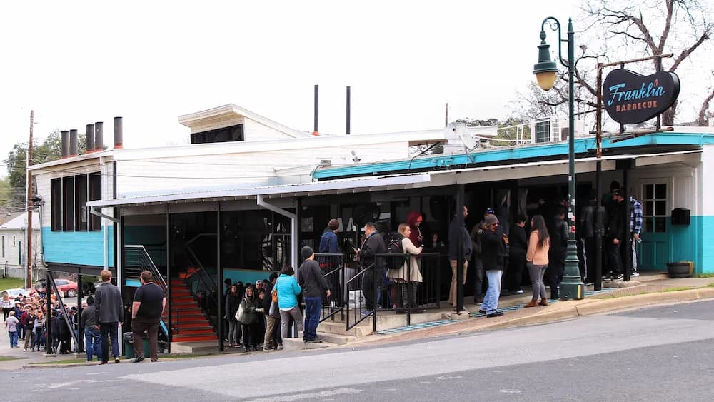 A long line of customers waiting outside Franklin Barbecue in Austin, Texas, showcasing the restaurant's popularity and success. Aaron Franklin has repeatedly emphasized that there will ever only be one Franklin BBQ pits.