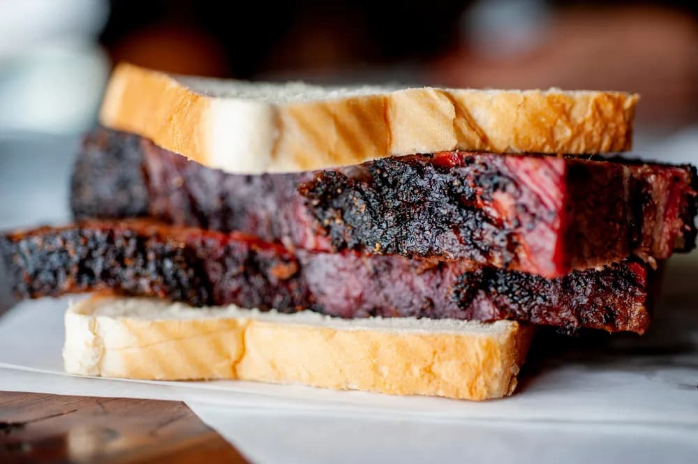 Slices of smoked brisket between two slice of white bread at Franklin BBQ. Aaron Franklin brisket continues to be a huge draw for barbecue enthusiasts from around the world.