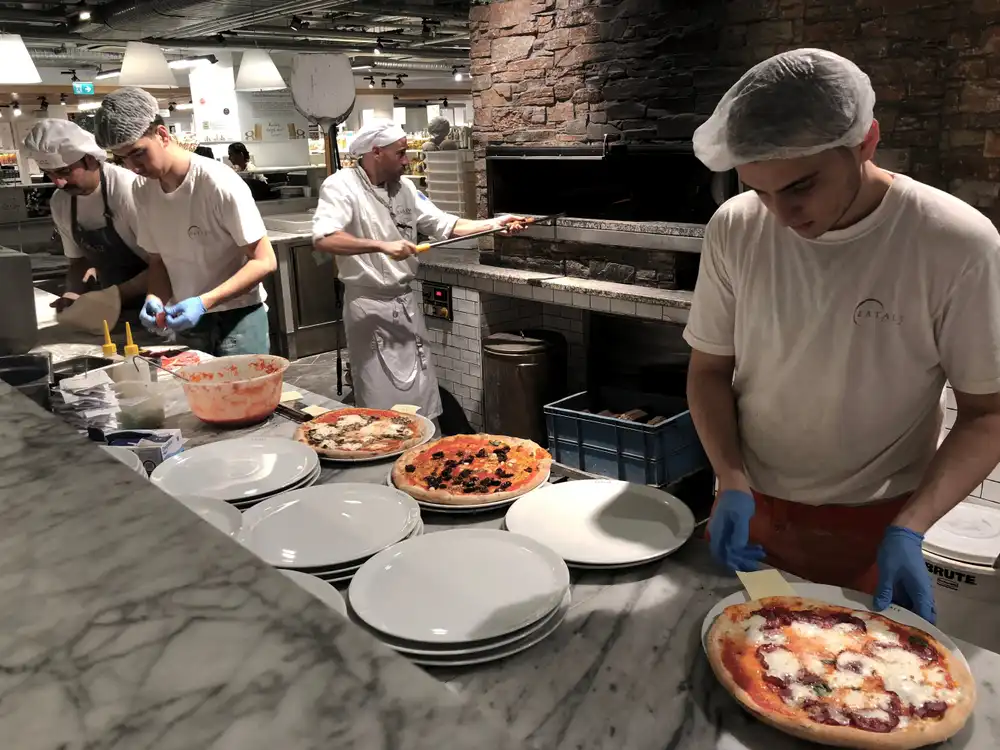 Trabajadores en una pizzería dentro de la ubicación de Eataly en Estambul, Turquía, preparan pizzas frescas, destacando el compromiso de Eataly con la auténtica cocina italiana en todo el mundo.